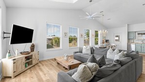 A spacious living room with a large grey sofa, a wooden coffee table, and a flat-screen TV mounted on the wall.
