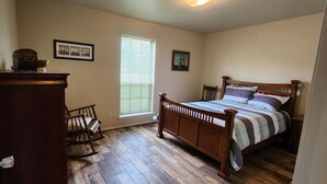 A bedroom with a wooden bed, a rocking chair, a dresser, and a window with blinds. - Peaceful Country Home, Pets,  Extended Stays (Rosharon)
