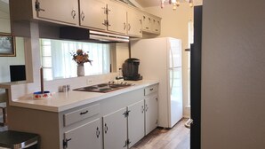 A kitchen with white cabinets, a stove, a refrigerator, and a window with a flower vase. - Peaceful Country Home, Pets,  Extended Stays (Rosharon)