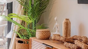 A modern living room with a large potted plant, a wooden console table with decorative items, and a television mounted on the wall.