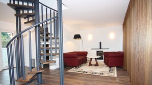 Un salon moderne avec un escalier en colimaçon, des canapés rouges, une table ronde et un plancher en bois.