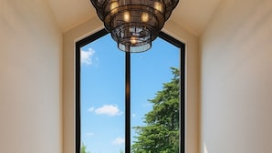 Un interior moderno con un ventanal grande, una escalera de madera y una barandilla de metal negro.