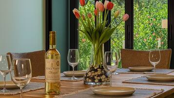 Een gedekte eettafel met wijnglazen, borden en een fles Vina Maipo wijn, met een vaas tulpen en uitzicht op groen buiten het raam.