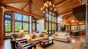 A spacious living area with large windows, wooden beams, and a chandelier.