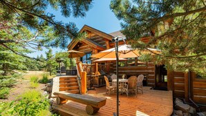 A log cabin with a deck, outdoor seating, and a large window overlooking the landscape.