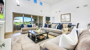 Un salón amplio con un gran ventanal corredera que da a un patio, un conjunto de sofás, una mesa de centro y un escritorio con una silla.
