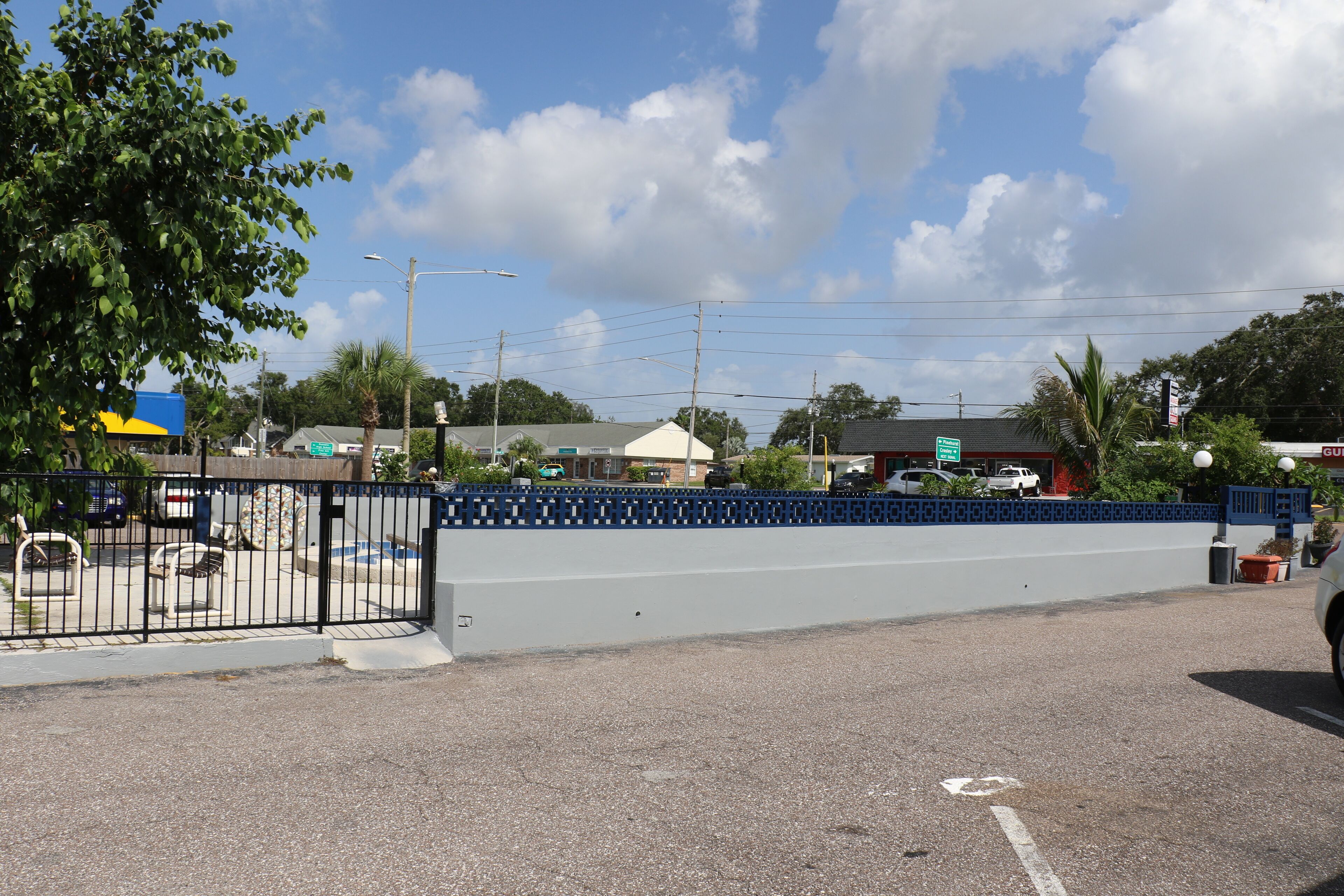 A parking lot with a blue fence, a tree, and a building in the background.