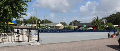 A parking lot with a blue fence, a tree, and a building in the background.