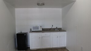 Cocina pequeña con armarios blancos, un microondas y un refrigerador.