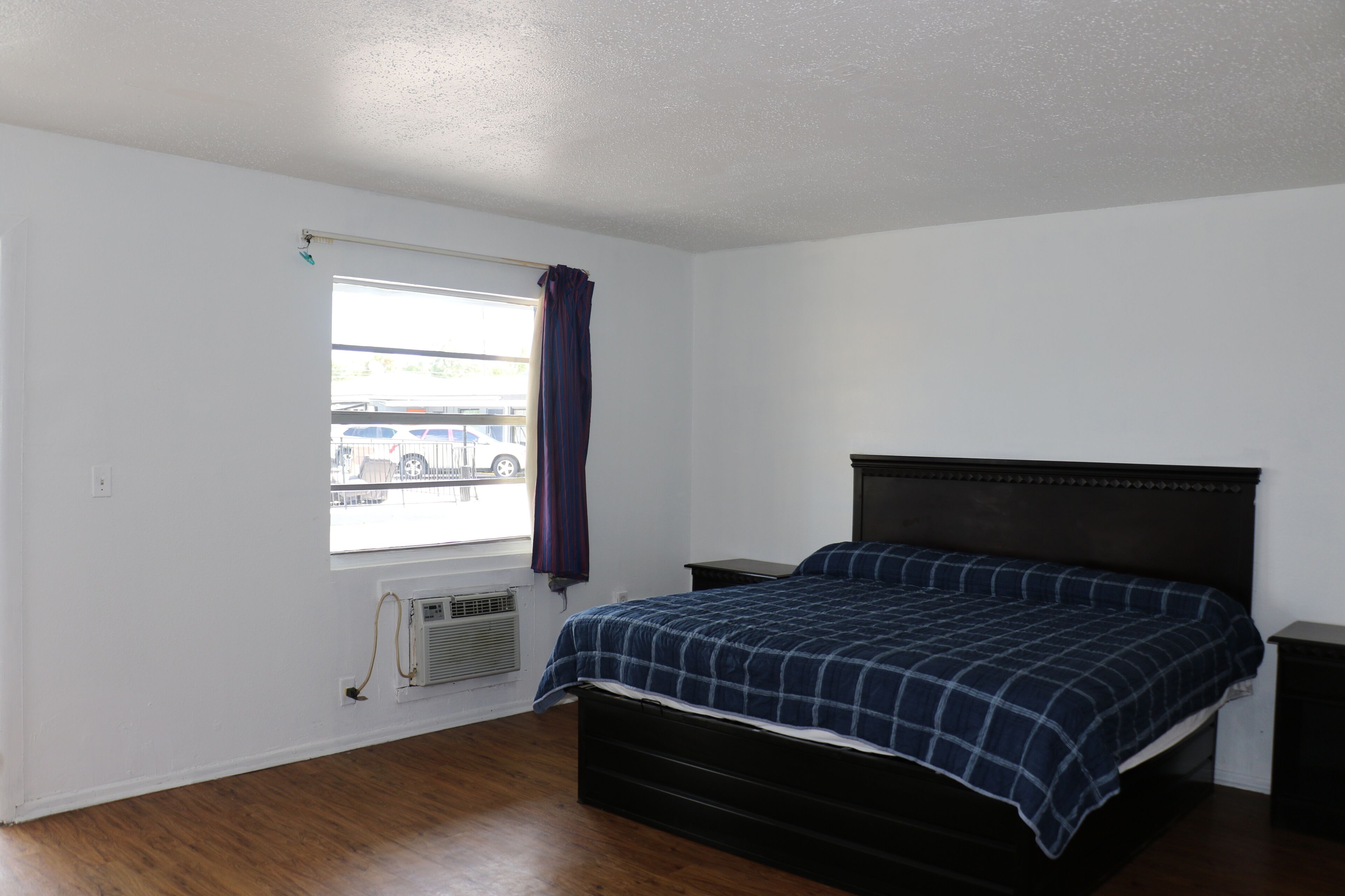 Un dormitorio con cama, ventana con cortina, calefactor y vista a un estacionamiento.