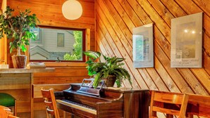 Une pièce chaleureuse avec un piano en bois, une table à manger, des chaises, une fenêtre donnant sur un beau paysage et deux tableaux encadrés accrochés au mur.