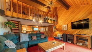 Un salon chaleureux avec un plafond en bois, un canapé vert, une table basse en bois et un téléviseur fixé au mur.