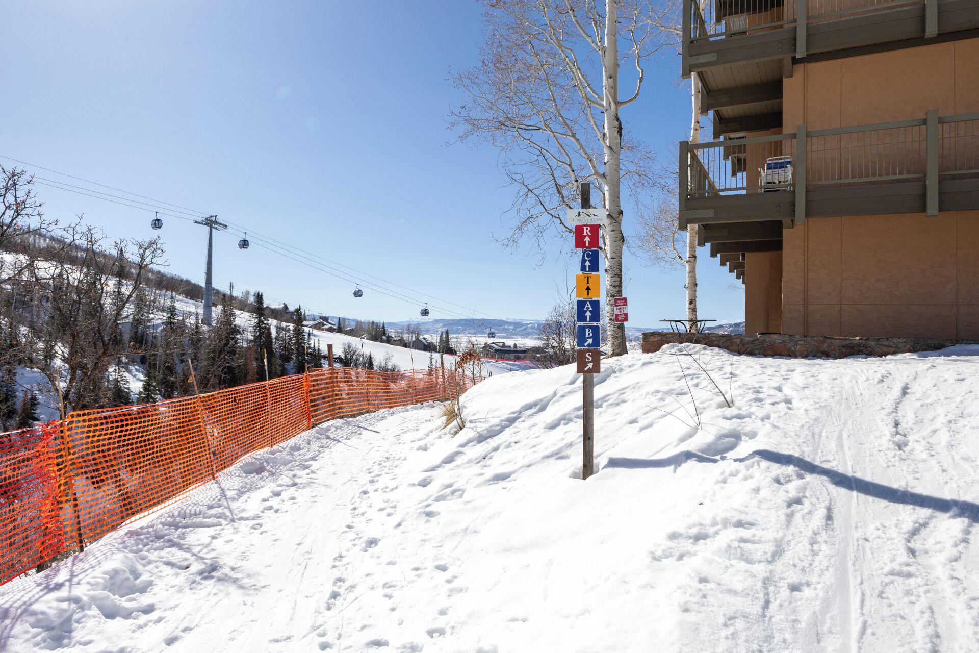 Une piste de ski enneigée, avec un panneau indicateur et une barrière de sécurité orange.
