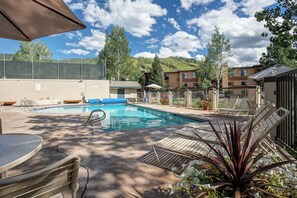 Une piscine entourée d’une clôture et d’arbres, avec des chaises longues et des parasols.