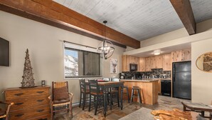 A kitchen with wooden cabinets, a black refrigerator, a dining area with wooden chairs, and a small wooden table. - Ski In Ski Out, Steps from the Slopes + Club Amenities (Steamboat Springs)