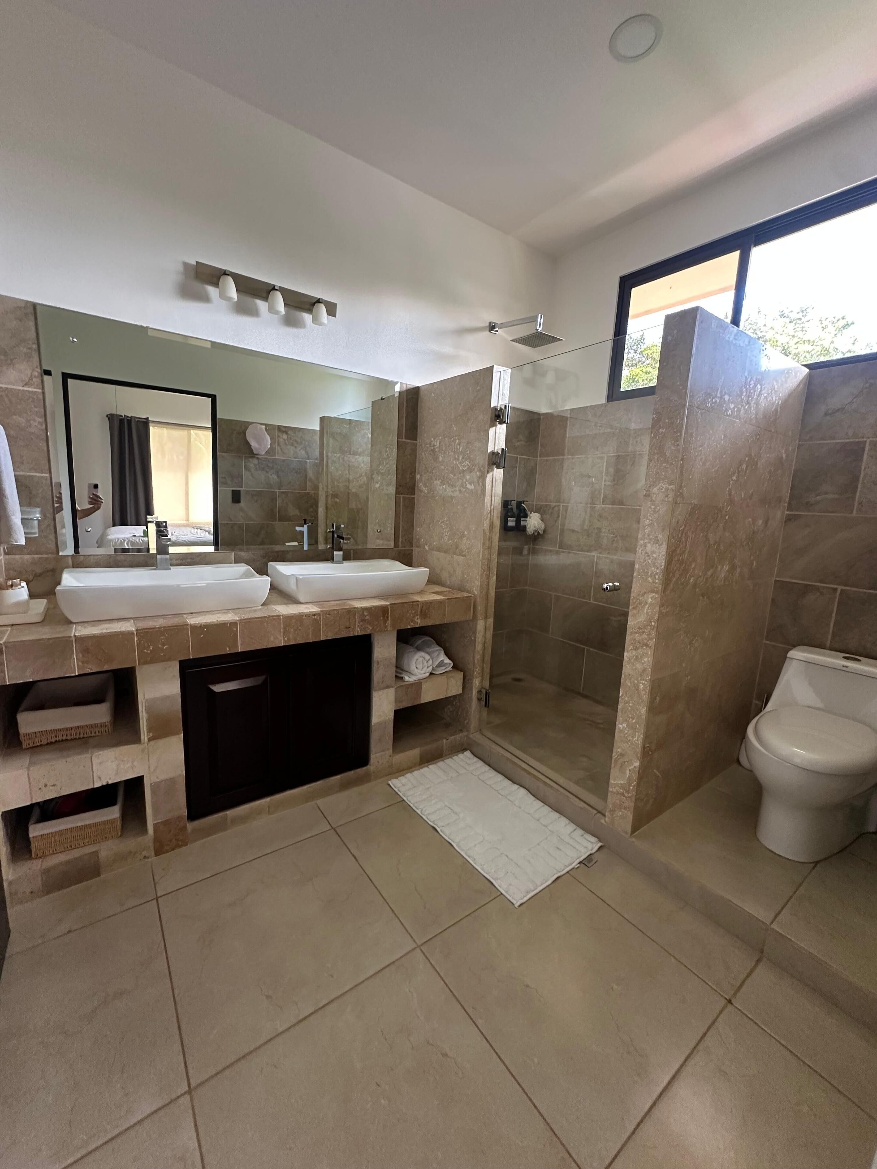 A modern bathroom with two sinks, a shower, and a toilet.