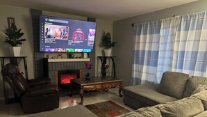 Una sala de estar con televisor de pantalla plana, sillón de cuero, sofá y chimenea.
