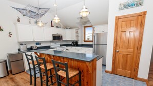 Una cocina con armarios blancos, una isla de madera con taburetes de bar, electrodomésticos de acero inoxidable e iluminación colgante.