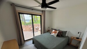 A bedroom with a bed, a nightstand, a desk, a ceiling fan, and a view of the outdoors through a sliding door.