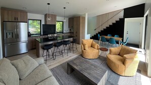 A modern kitchen with a central island, stainless steel appliances, and a dining area with blue chairs.