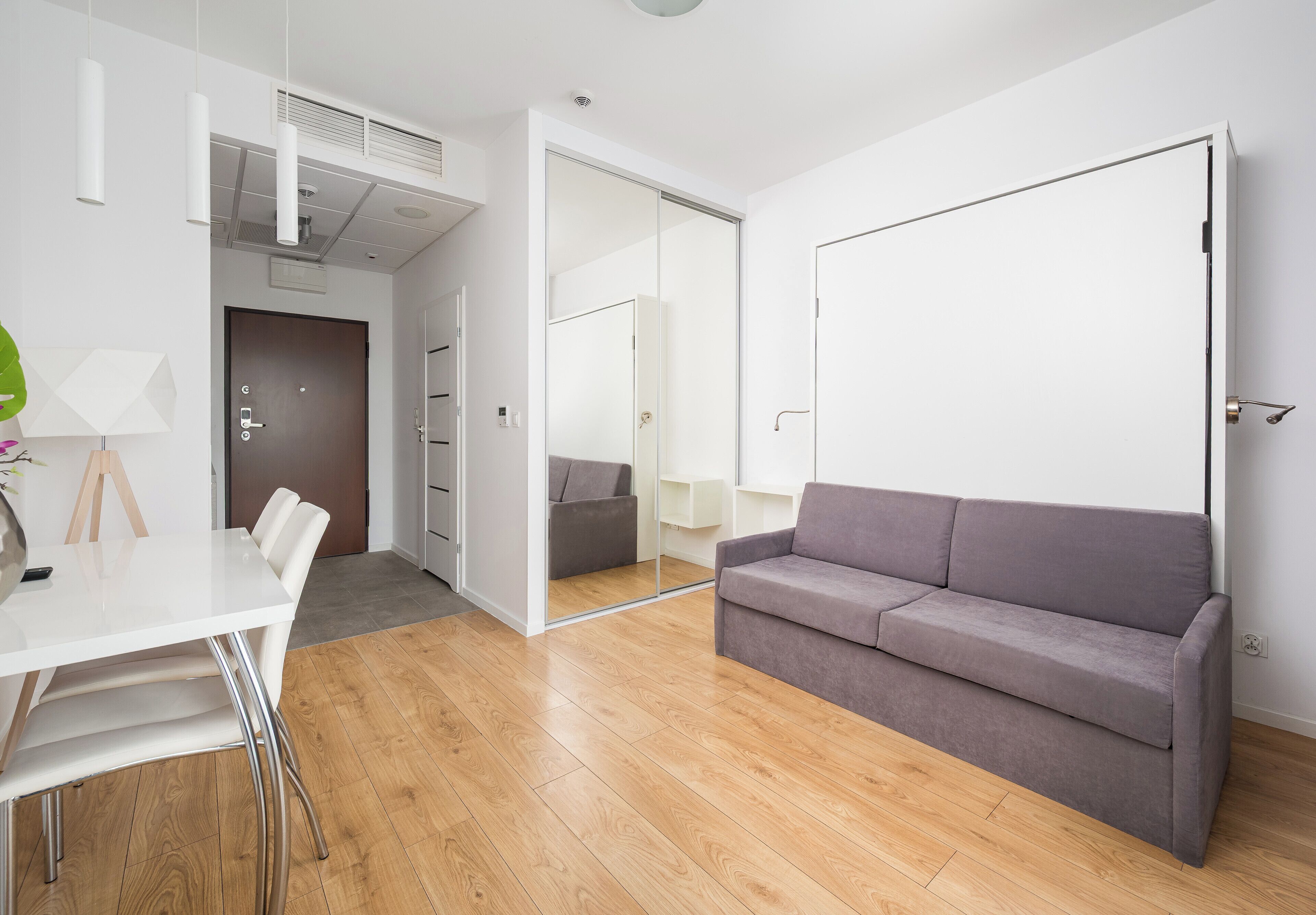 Ein modernes Wohnzimmer mit weißem Tisch, grauem Sofa und Holzboden.