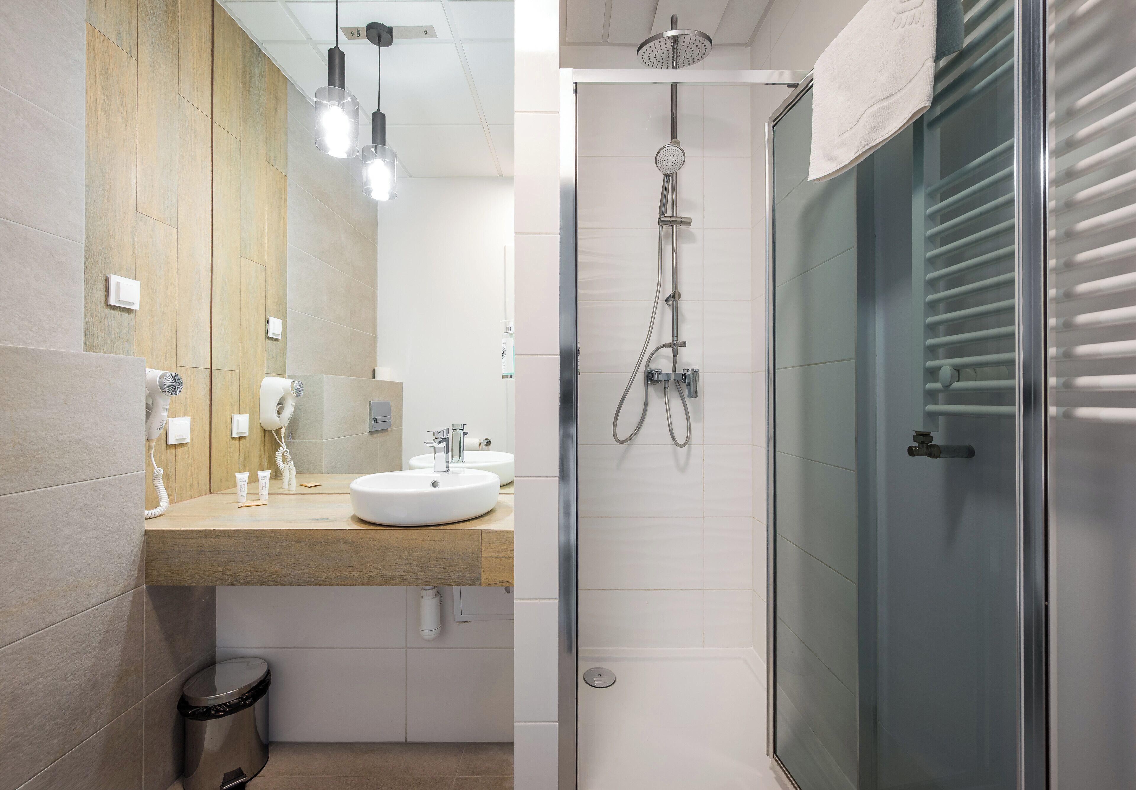 A modern bathroom with a wooden vanity, a glass shower enclosure, and a white sink.