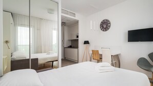A hotel room with a large bed, a desk, a chair, a TV, a clock, and a view of the kitchen and balcony. - Varsovia Comfort 922 (Warszawa)