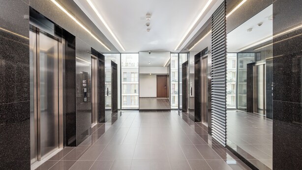 A modern elevator lobby with glass doors, a tiled floor, and a ceiling with recessed lighting.