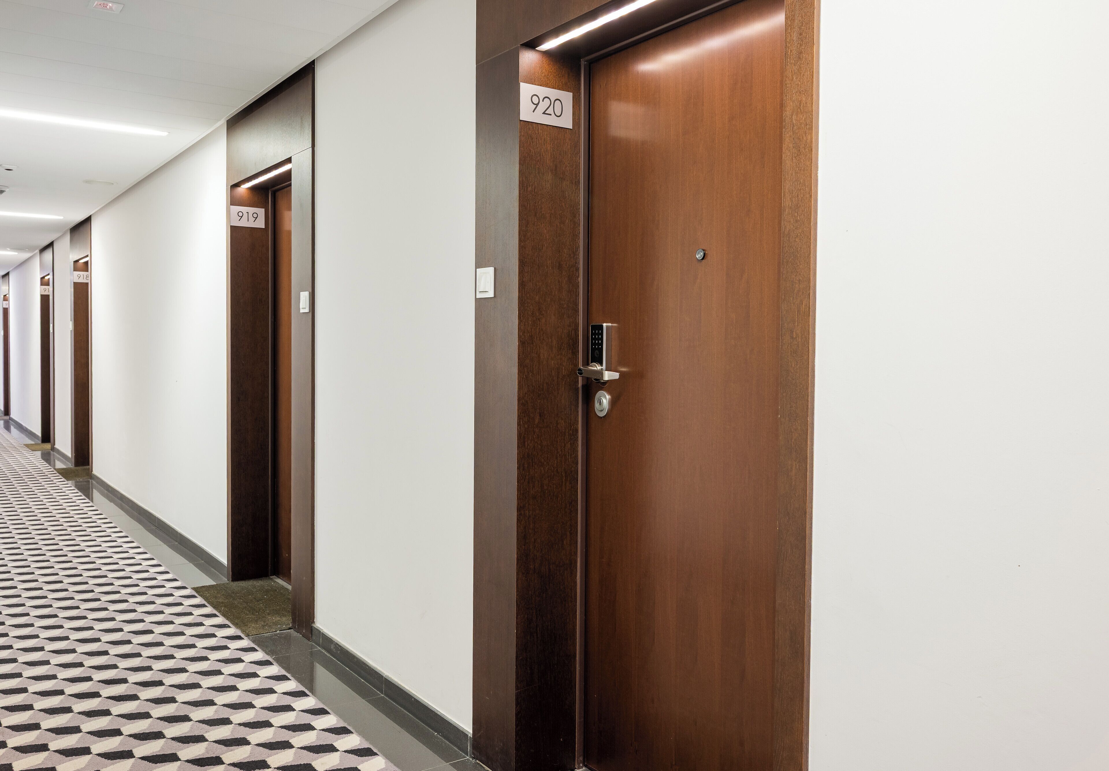A hotel corridor with wooden doors, numbered signs, and a patterned floor.