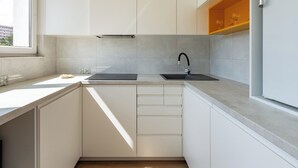 A modern kitchen with white cabinets, a black sink, and a window providing natural light. - Lecha Comfort Apartment (Gdańsk)