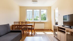 A modern apartment with a sofa, dining table, chairs, a TV, and large windows. - Lecha Comfort Apartment (Gdańsk)
