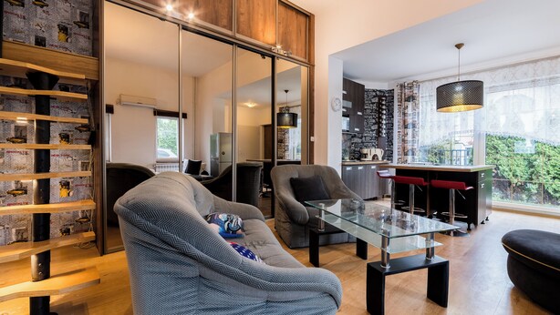 Una sala moderna con una mesa de centro de vidrio, un sofá, un comedor con sillas rojas, y una cocina visible a través de una puerta corrediza.