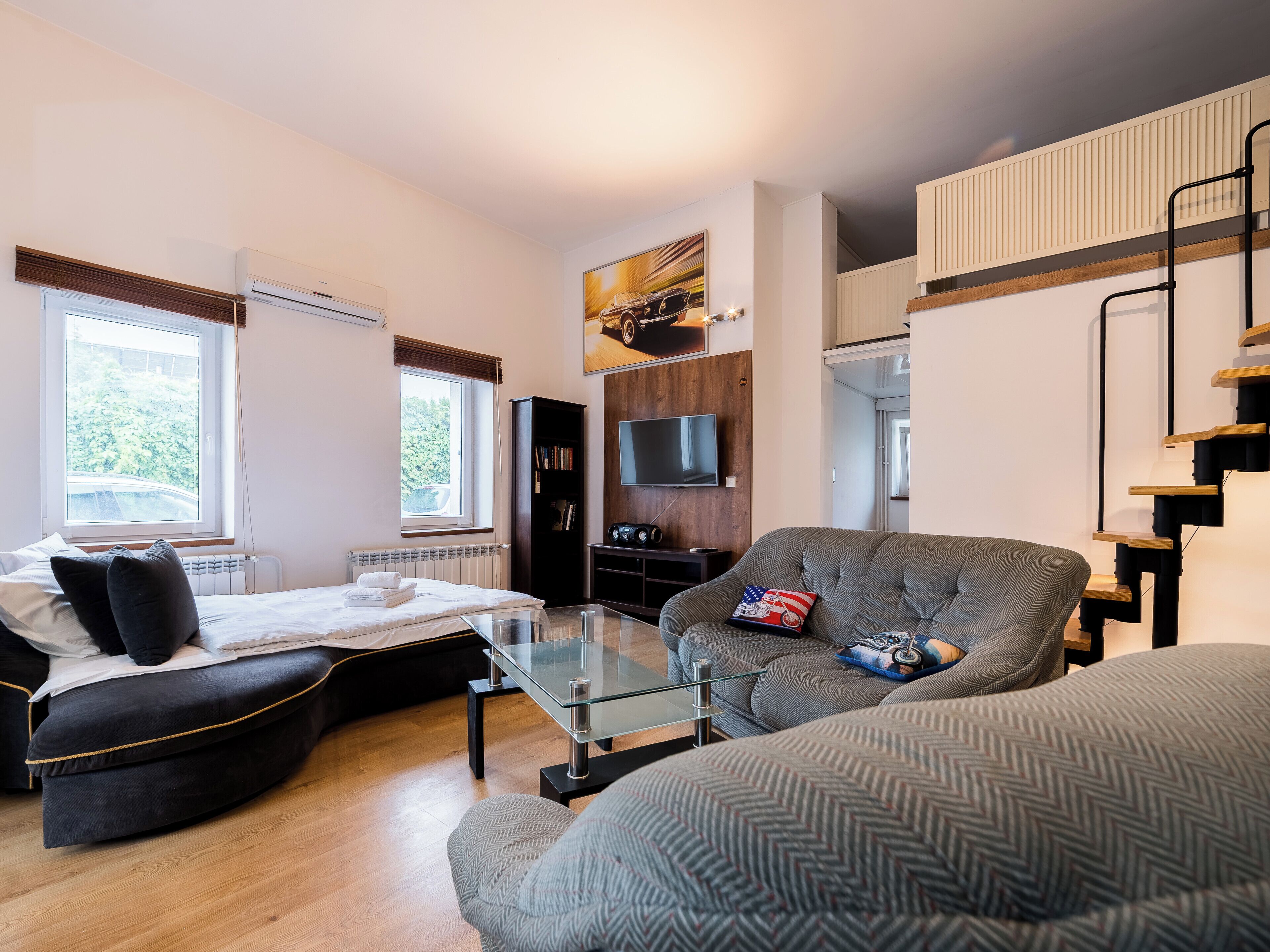 Een moderne woonkamer met een bank, een glazen salontafel, een zwarte boekenkast en een aan de muur bevestigde televisie.