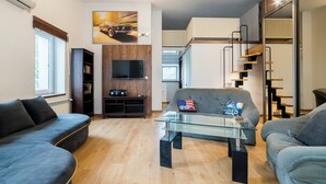 Una sala de estar moderna con un sofá, una mesa de centro de vidrio, un televisor montado en una pared de madera y una escalera que lleva a un nivel superior.