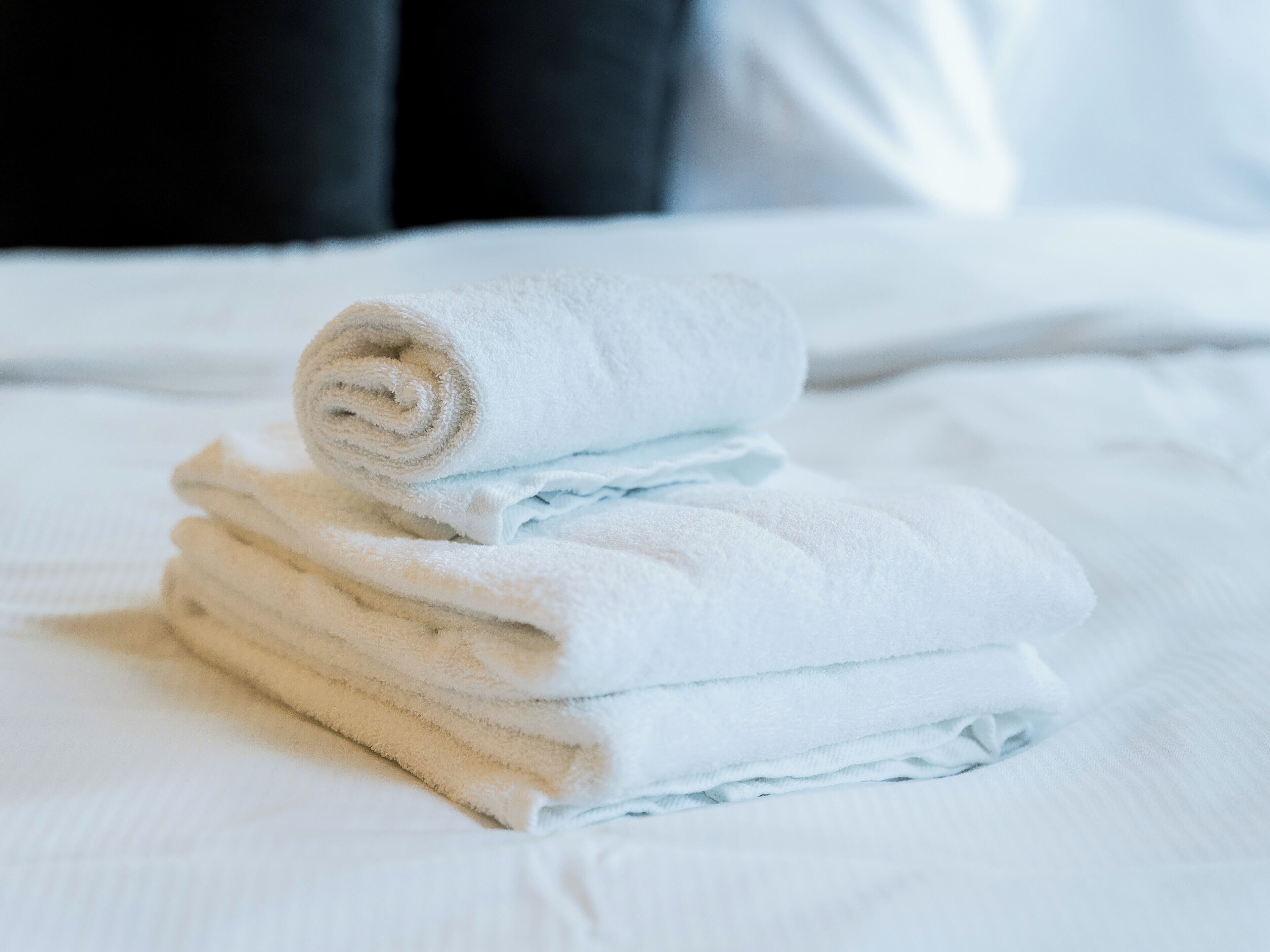 Un montón de toallas blancas dobladas con cuidado sobre una cama con sábanas blancas.