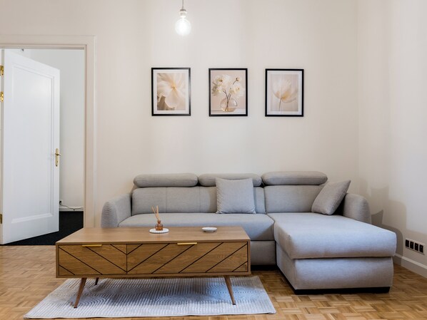 A modern living room with a grey sectional sofa, a wooden coffee table, and three framed floral artworks on the wall.
