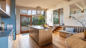 A modern kitchen with a central island, wooden flooring, and large windows offering a view of the outdoors.