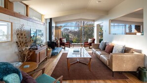 A spacious living room with a fireplace, comfortable seating, and large windows offering a view of the outdoors.