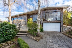 Ett modernt hus i två våningar med ett garage, en trappa som leder upp till entrén och en välskött trädgård.