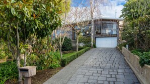 A paved pathway leading to a modern house with a garage, surrounded by lush greenery and trees.