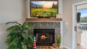 A fireplace with a TV above it, a potted plant, and a view of a balcony.