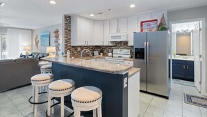 A modern kitchen with a central island, bar stools, stainless steel appliances, and a stone backsplash.