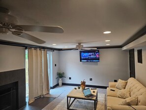 A modern living room with a flat-screen TV mounted on the wall, a ceiling fan, and a sofa.