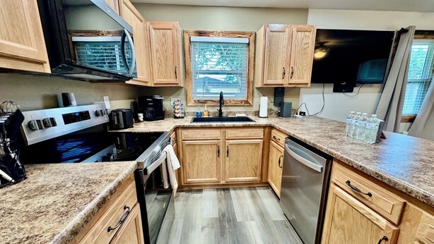 A kitchen with wooden cabinets, a stainless steel range, a dishwasher, and a window with a view. - Drew’s Delight - Relax in Comfort!  Modern, Fully Remodeled, No Stairs! (Mountain Grove)