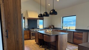 A modern kitchen with wooden cabinets, a large island, and pendant lighting. - Cozy, Tranquil, & Stunning Lake View Home with Hot Tub, Sauna, and Outdoor Fun! (Elmo)