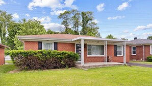 A single-story brick house with a covered porch, a small front yard, and a clear blue sky. - Cozy 3BR Getaway  Pets OK + Fenced Yard (Jeffersonville)