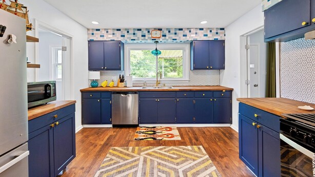 A modern kitchen with dark blue cabinets, a stainless steel dishwasher, a wooden countertop, and a patterned rug. - Cozy 3BR Getaway  Pets OK + Fenced Yard (Jeffersonville)