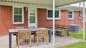 A covered patio with a brick building, a table with chairs, and a bench. - Cozy 3BR Getaway  Pets OK + Fenced Yard (Jeffersonville)