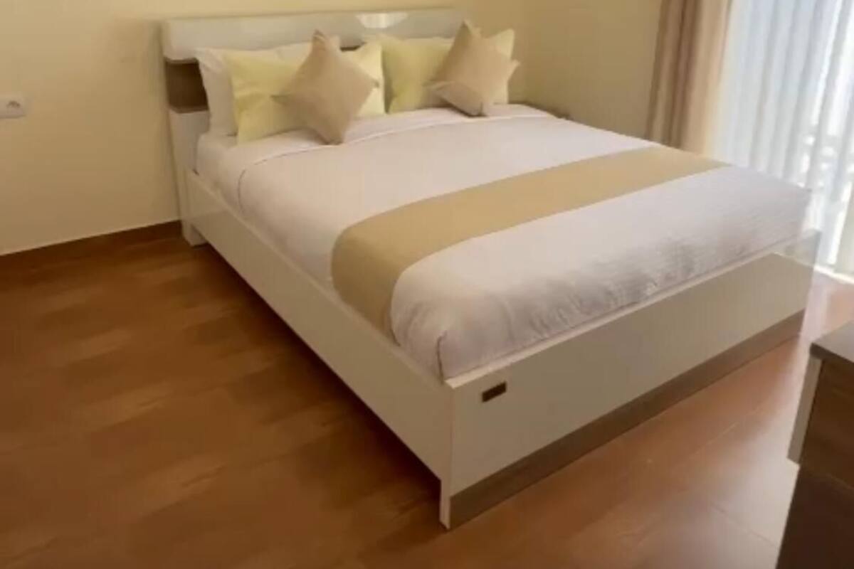 A neatly made bed with a white and beige bedspread, a wooden headboard, and several pillows.