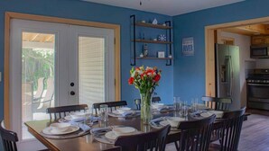 A dining room with a table set for six, a ceiling fan, and a kitchen area visible through an open door. - The Crossmon House (Alexandria Bay)